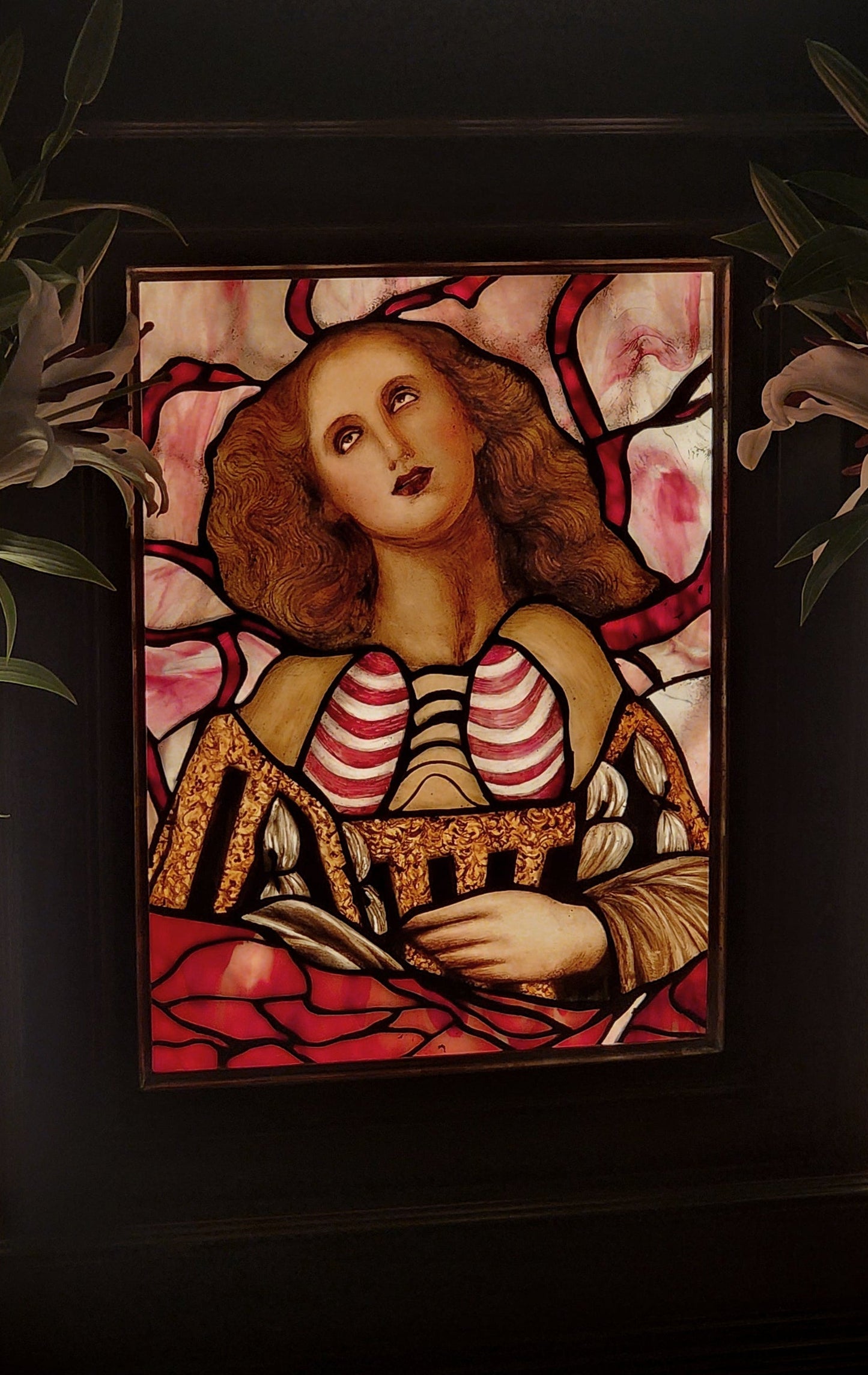 Stained glass artwork of a woman with a red background, placed on a dark surface.